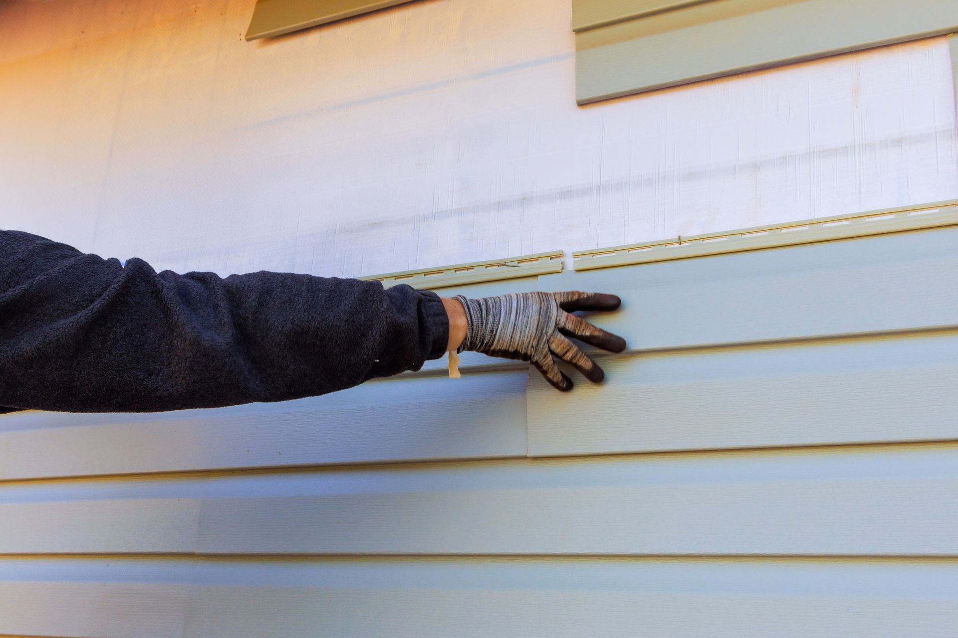 Gloved hand applying or inspecting white horizontal siding on a house wall