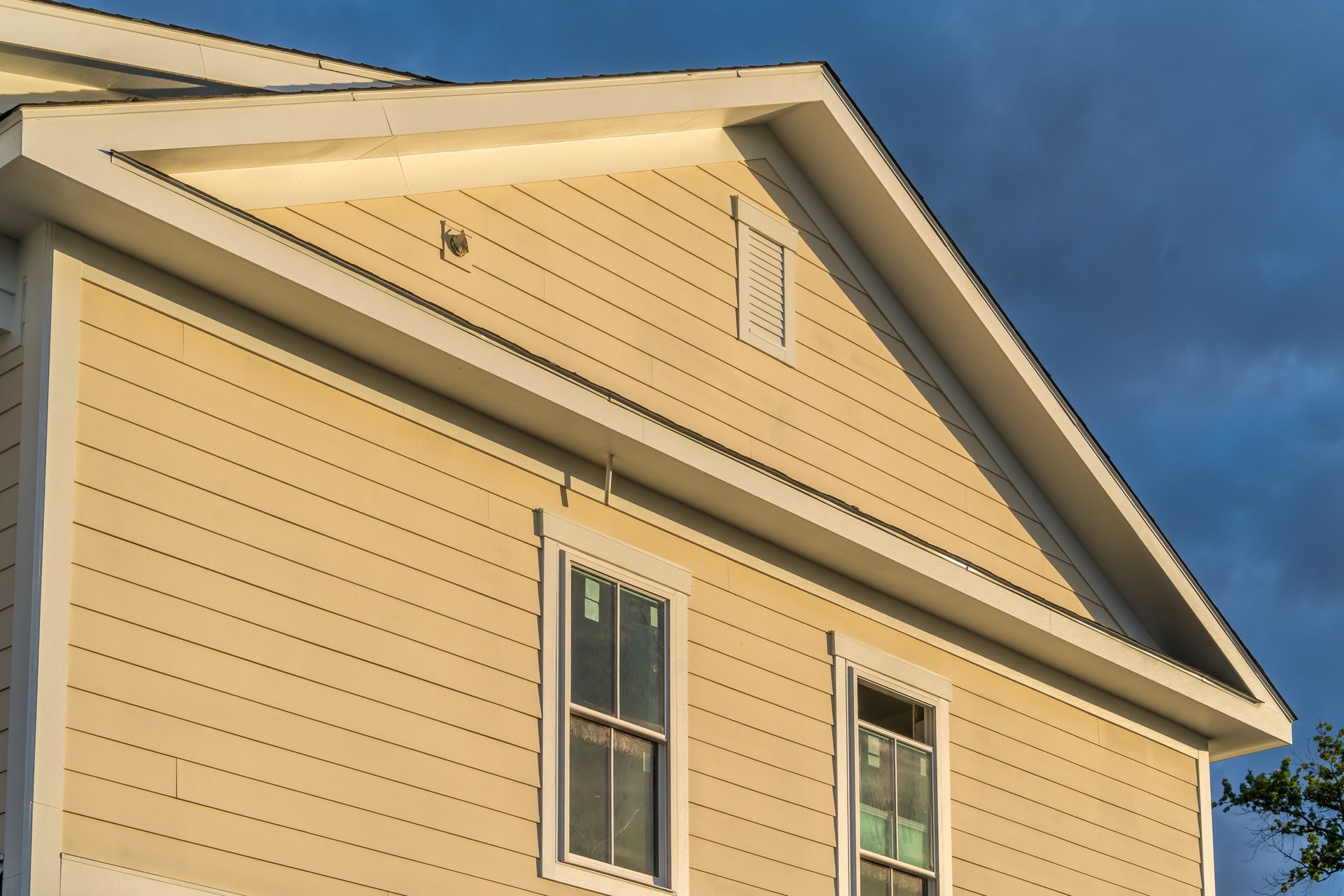 Sunlit beige house siding and roofline against a blue sky