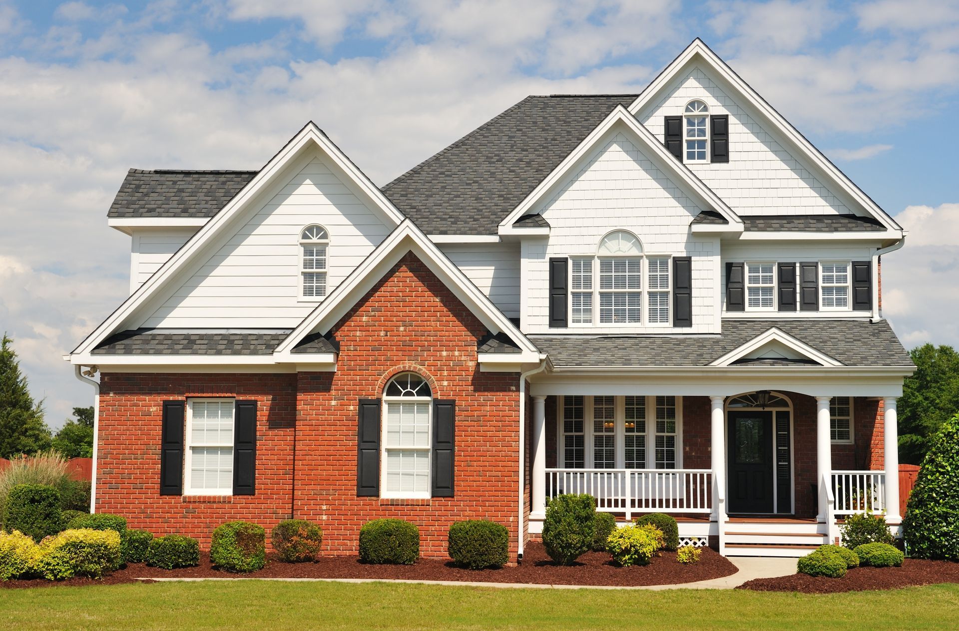 Large two-story suburban house with red brick, white siding, black roof, and a front porch.