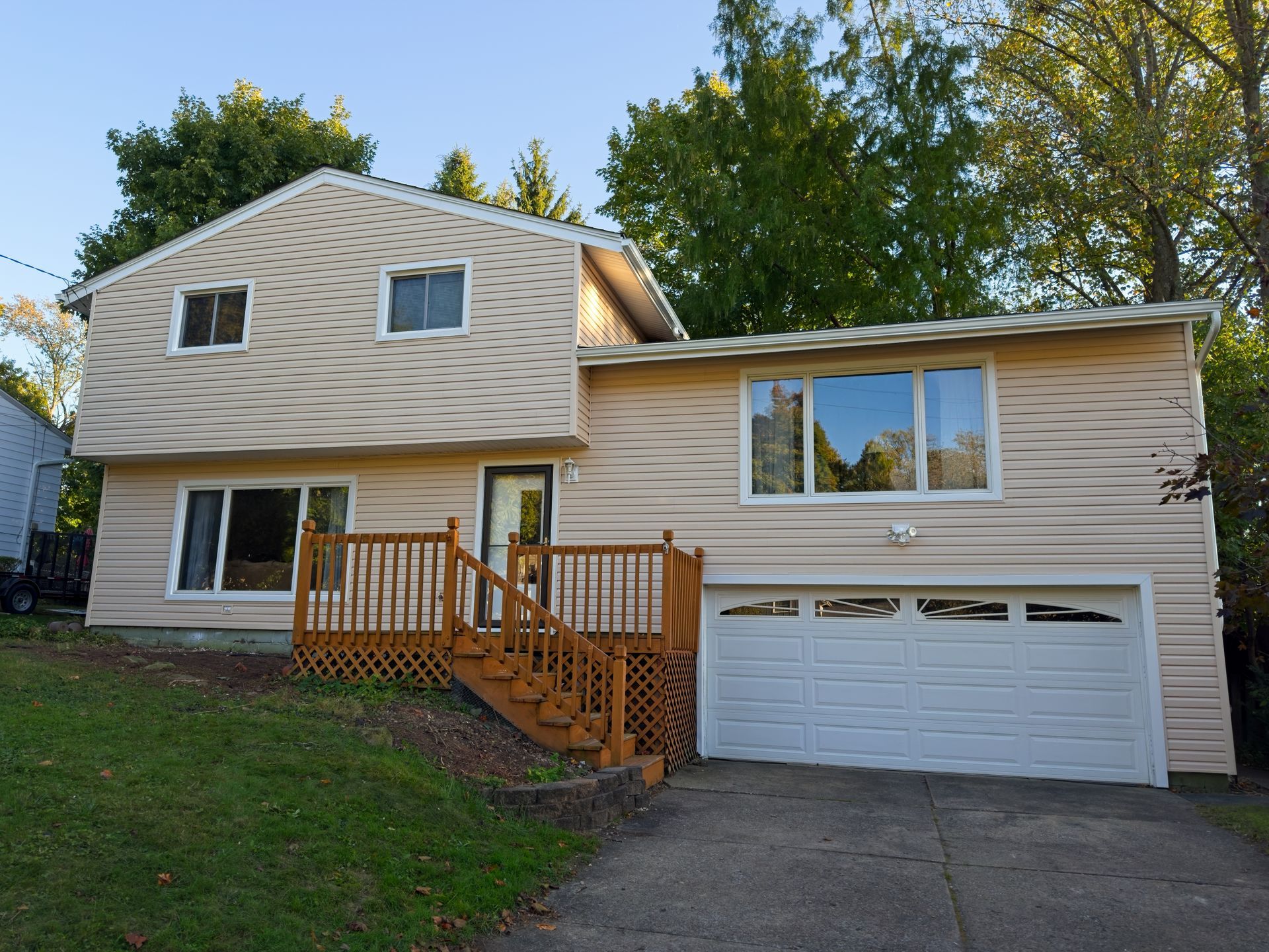 Suburban house exterior with beige siding, wooden front steps, and a two-car garage at dusk