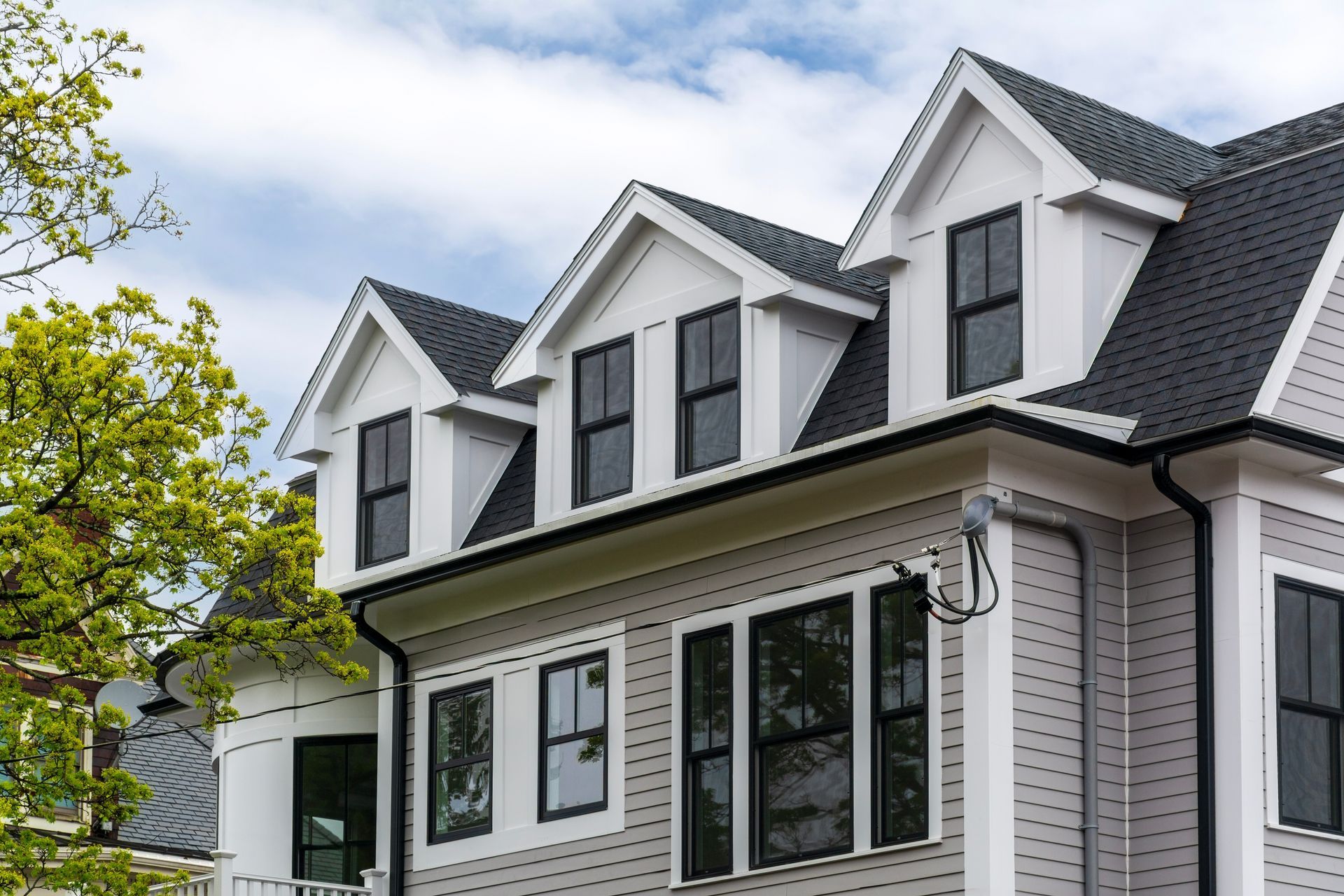 White house exterior with dormer windows, black shutters, and a leafy tree beside it