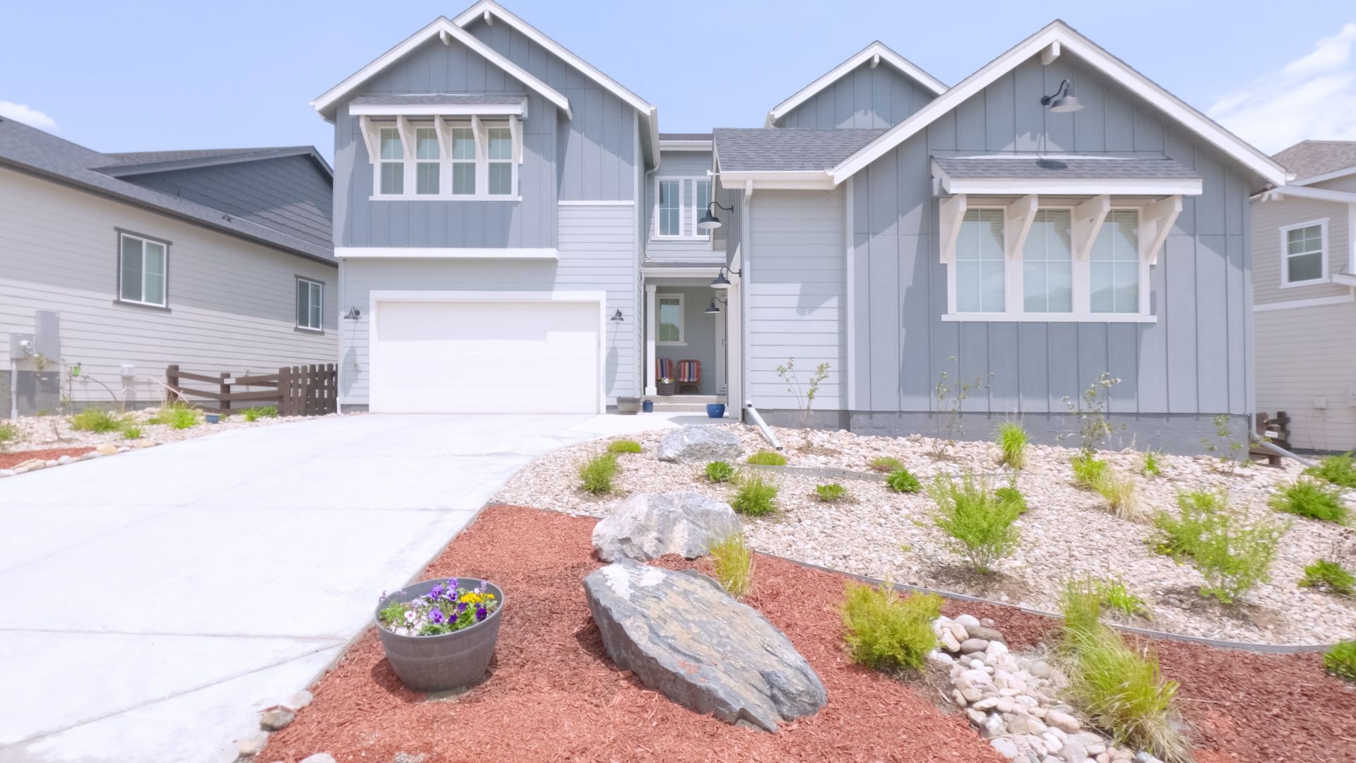 Modern gray suburban house with white trim, garage, and landscaped front yard with rocks and flowers