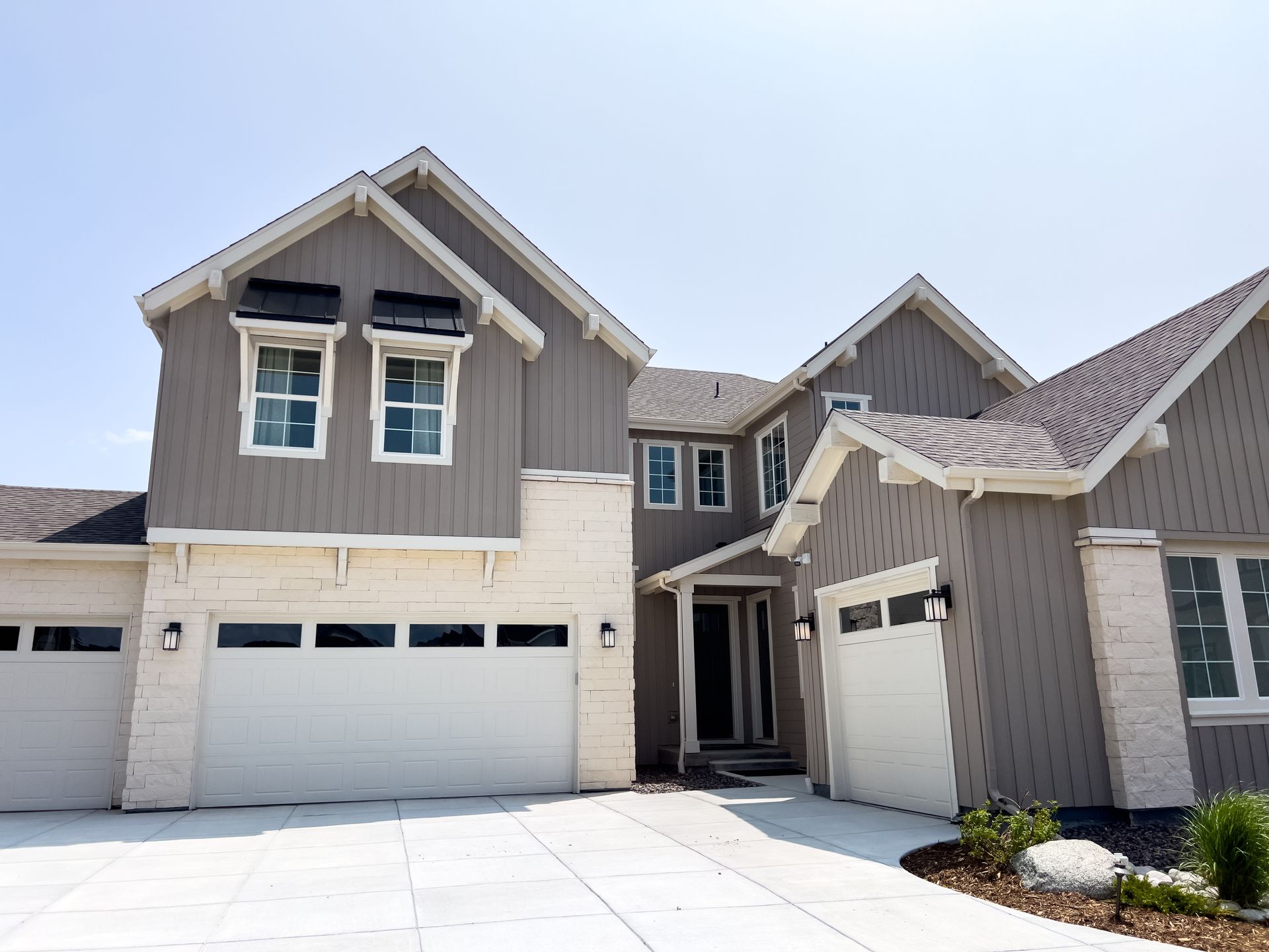 Modern two-story gray and beige suburban house with a three-car garage and snowy driveway