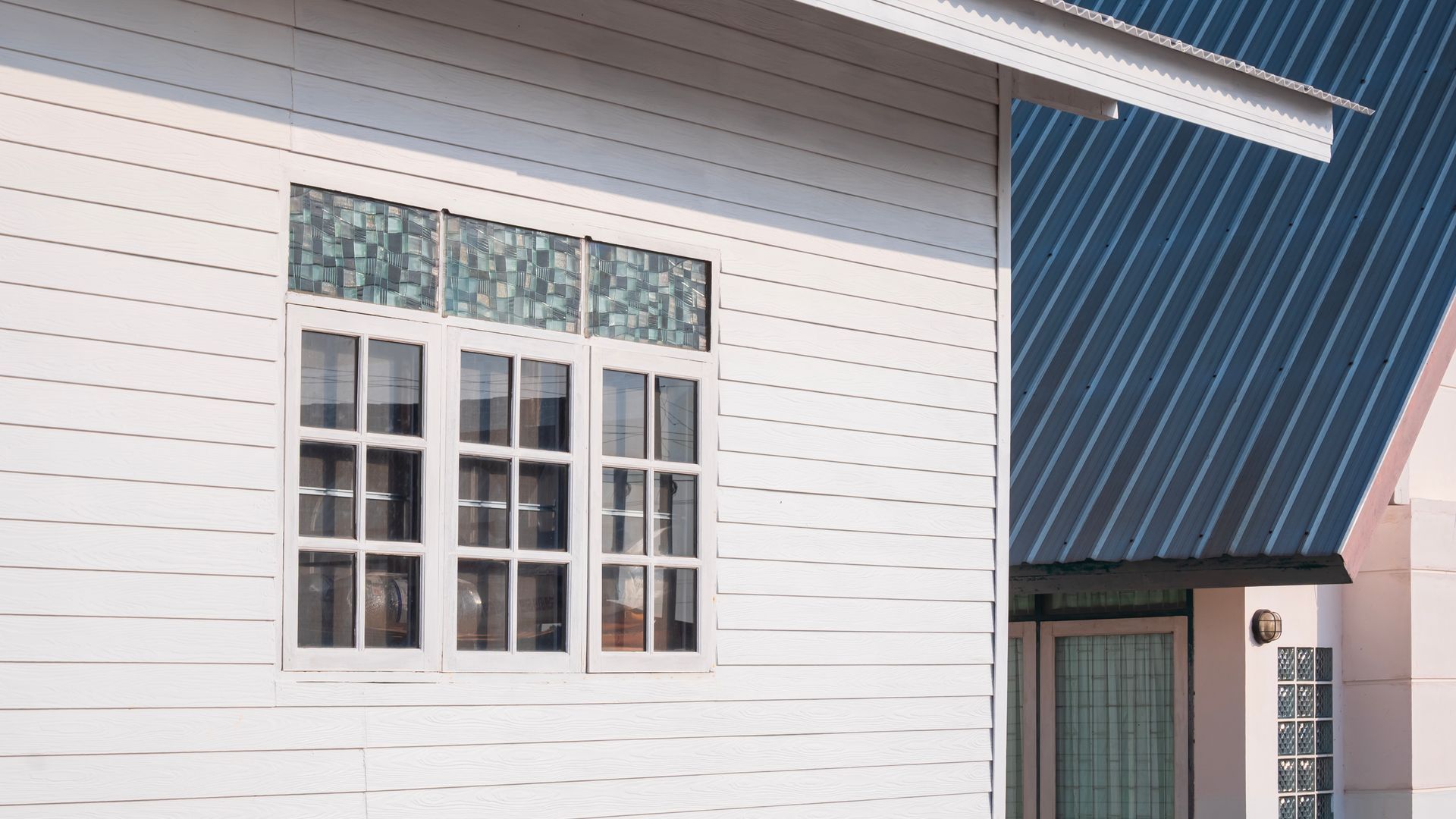 White building facade with a multi-pane window and blue metal roof edge above a doorway