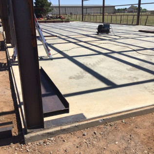 Construction site with steel frame structure over concrete slab. Sunlight casts shadows on the floor.