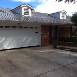 House exterior with brick accents, a white garage door, and a metal roof under a partly cloudy sky.