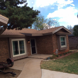Brick house with brown roof, porch, and a sidewalk leading to the front door.