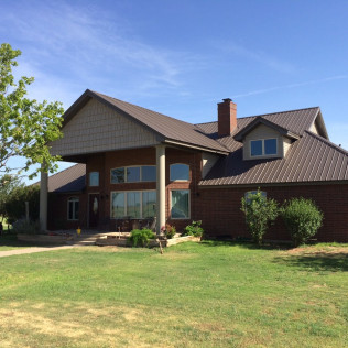 Brown house with metal roof on a green lawn under a blue sky.