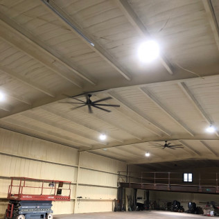 Large interior view of a building with light brown ceiling. Ceiling fans and bright lights are visible.
