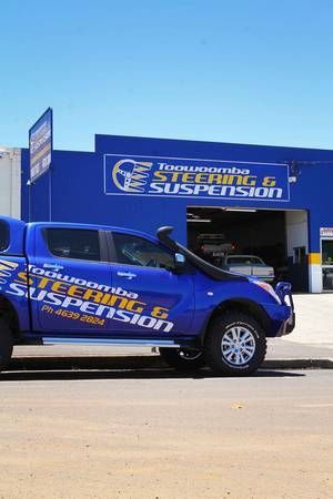 Blue pickup truck parked in front of Toowoomba Steering & Suspension shop with blue exterior and matching branding.