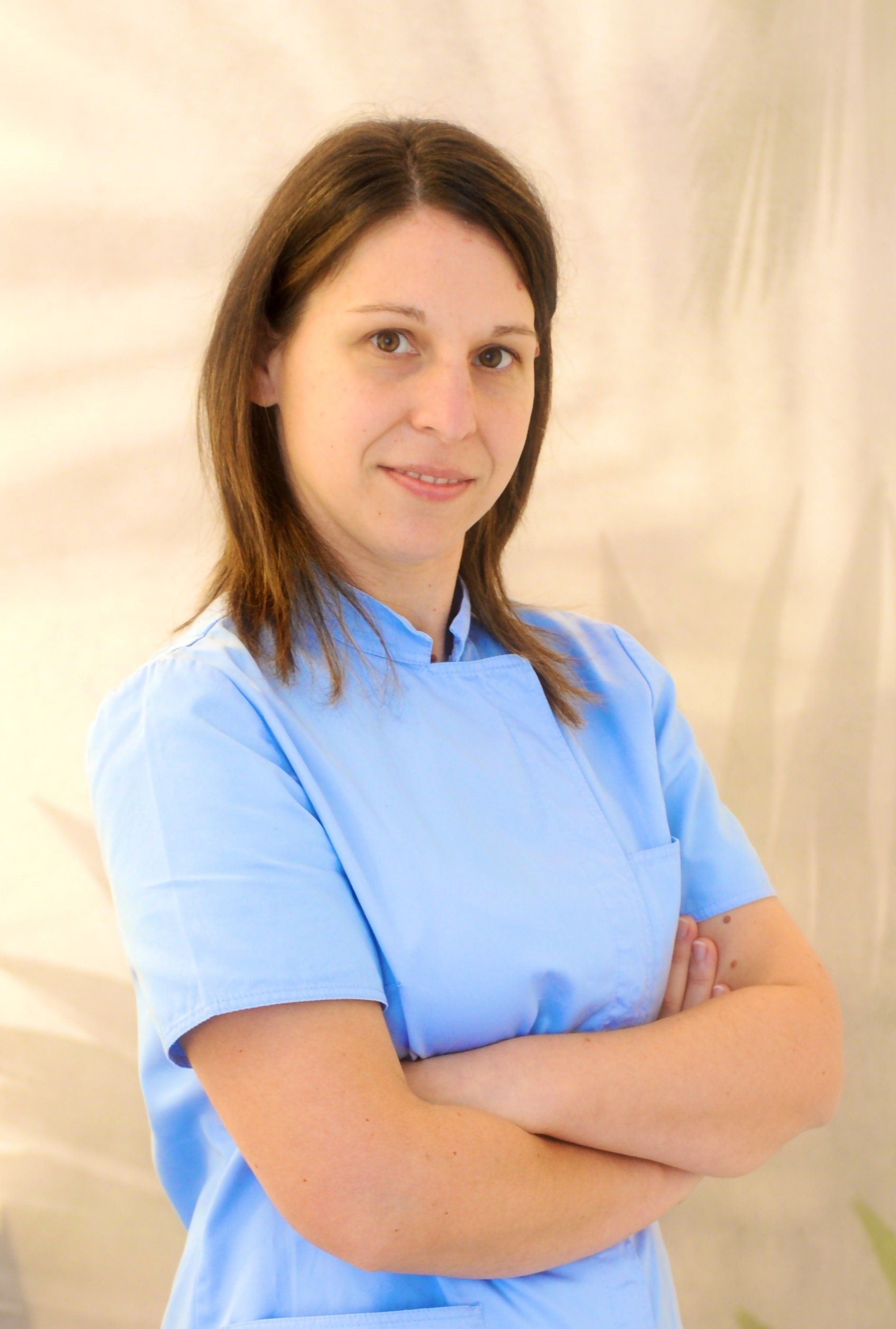 Una donna con un camice blu è in piedi con le braccia incrociate.