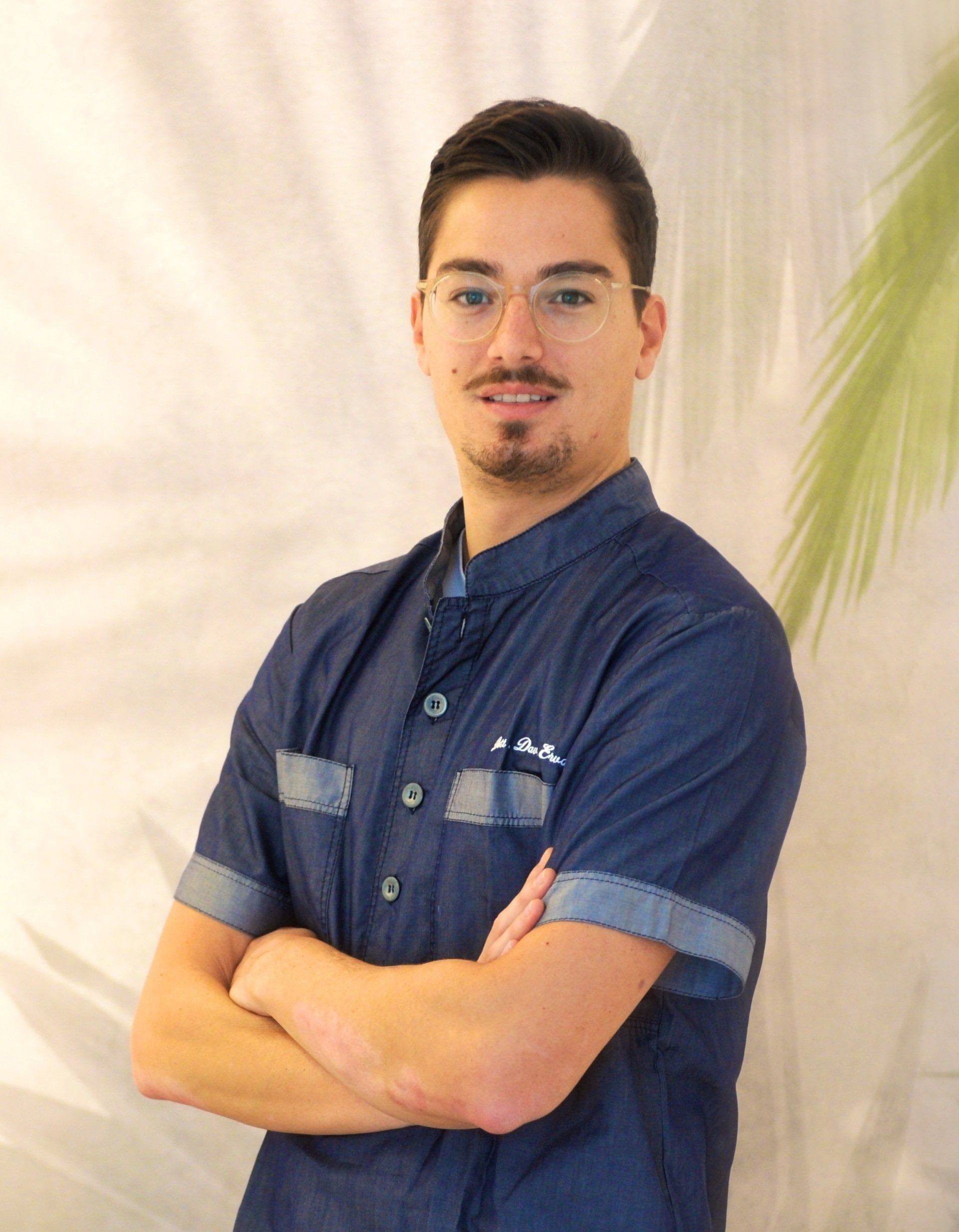 Un uomo con una camicia blu e gli occhiali è in piedi con le braccia incrociate.