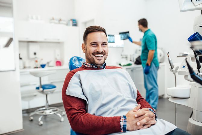 Un uomo sorride seduto sulla poltrona del dentista.