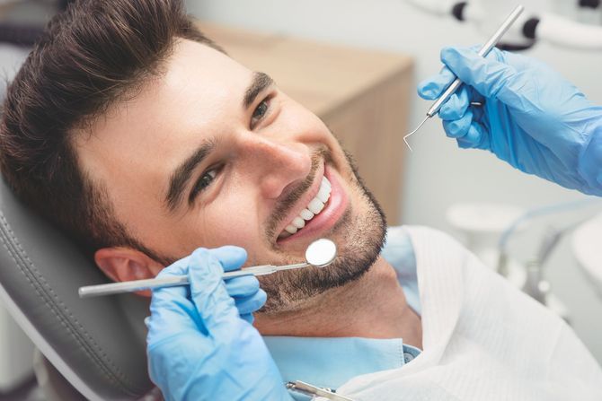Un uomo è seduto sulla poltrona del dentista mentre un dentista gli esamina i denti.