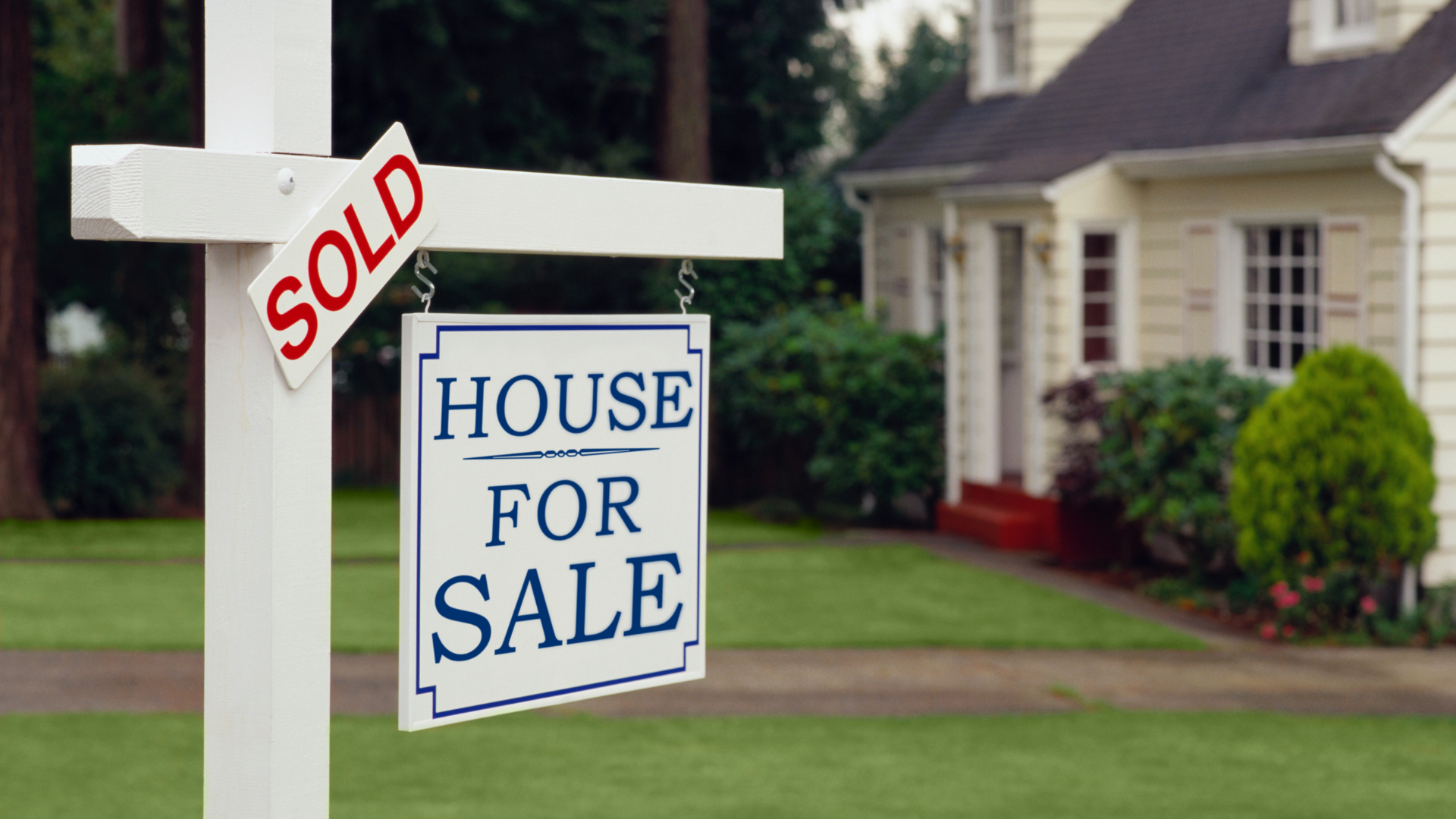 House for sale sign in front of a suburban home, with a red sold tag.