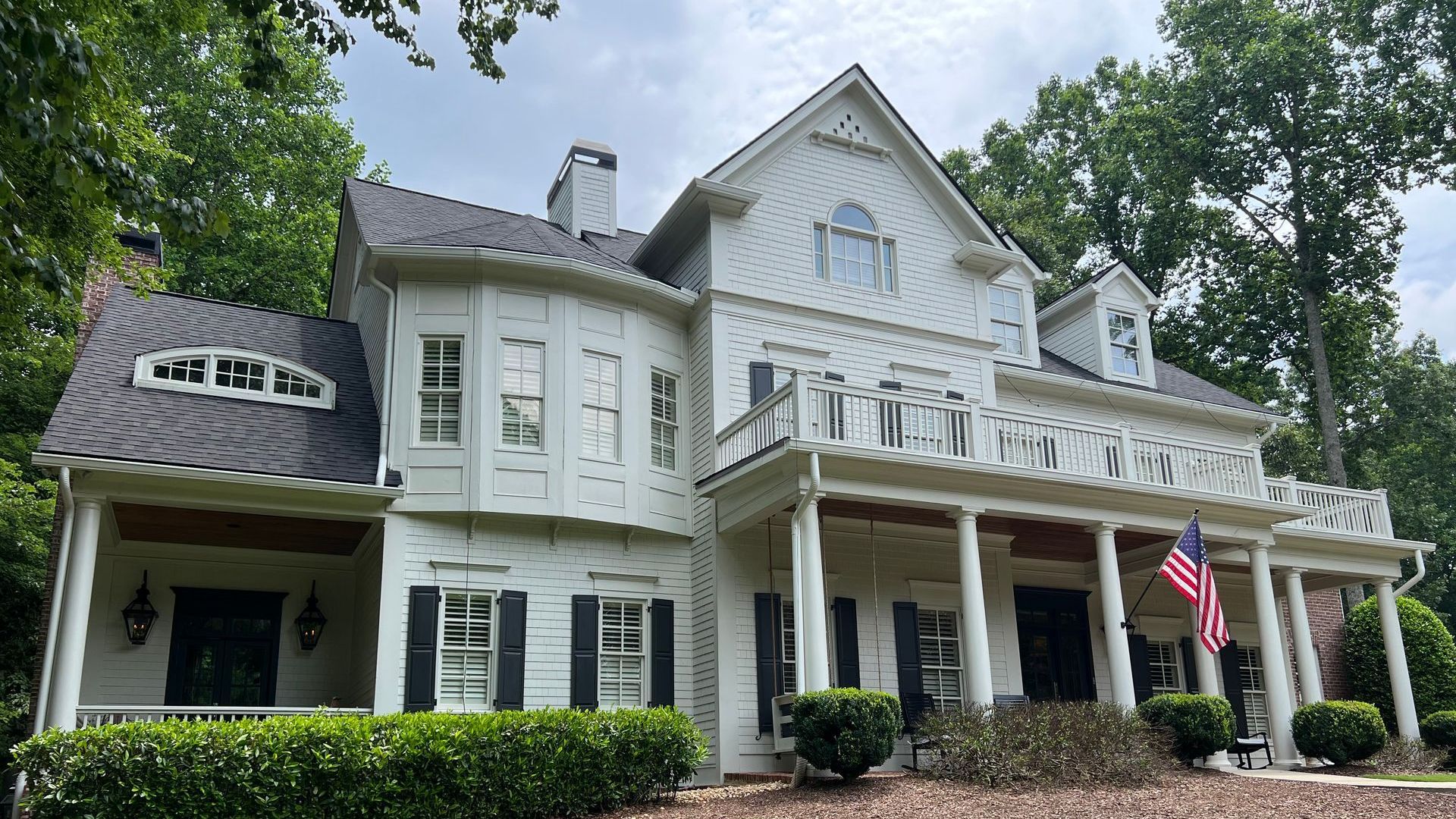 A large white house with a large porch and an american flag in front of it.