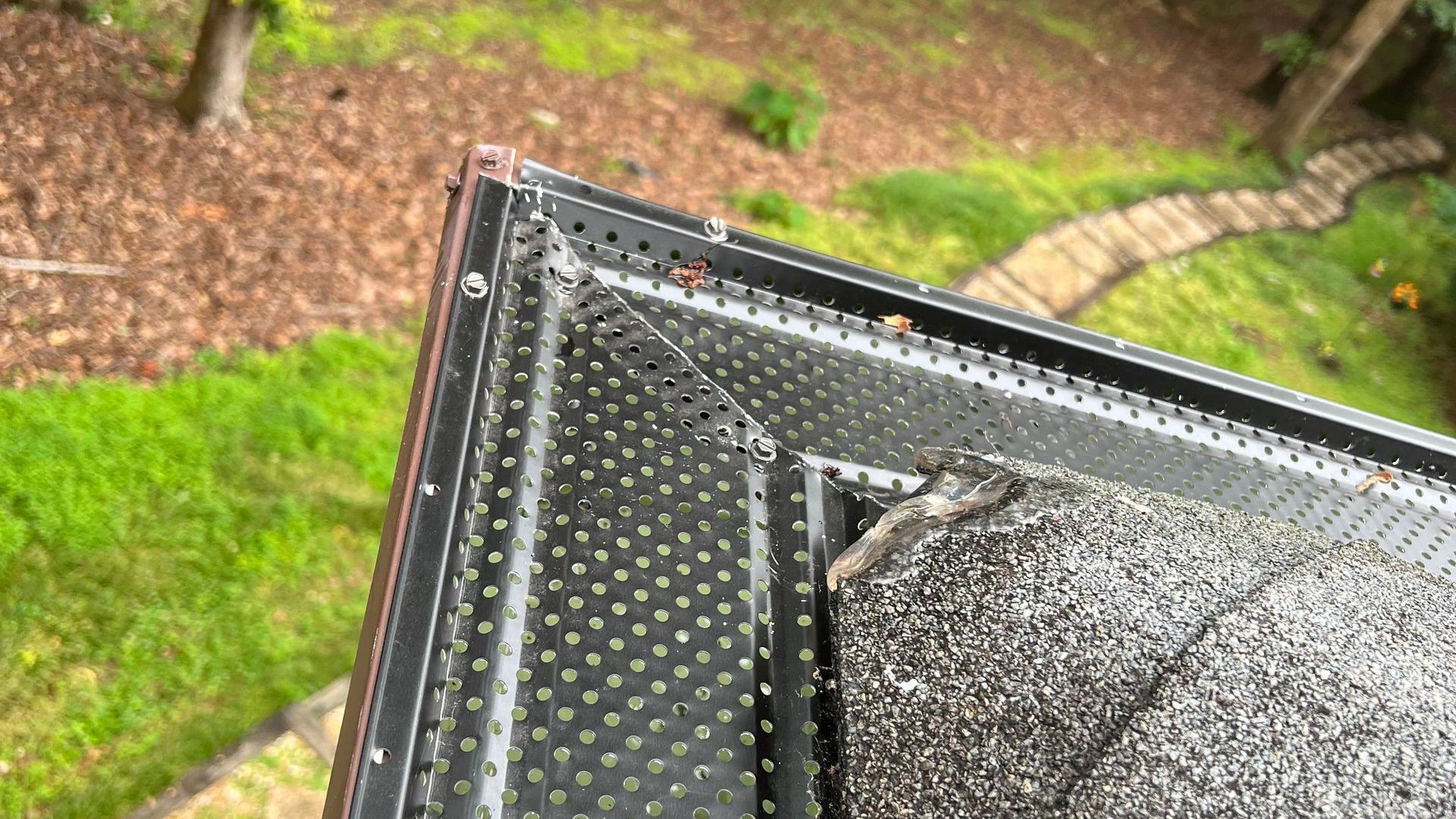 A close up of a gutter on a roof with a path in the background.