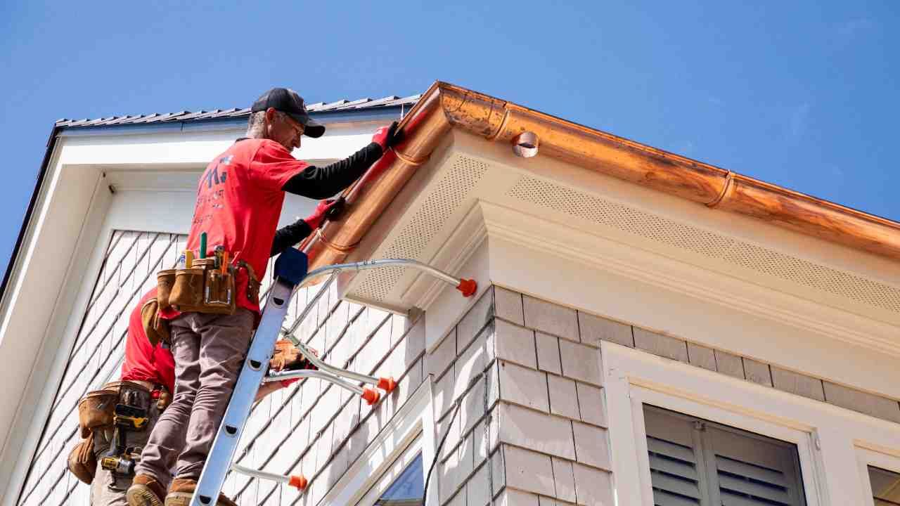 Worker painting the roof trim of a white house on a ladder