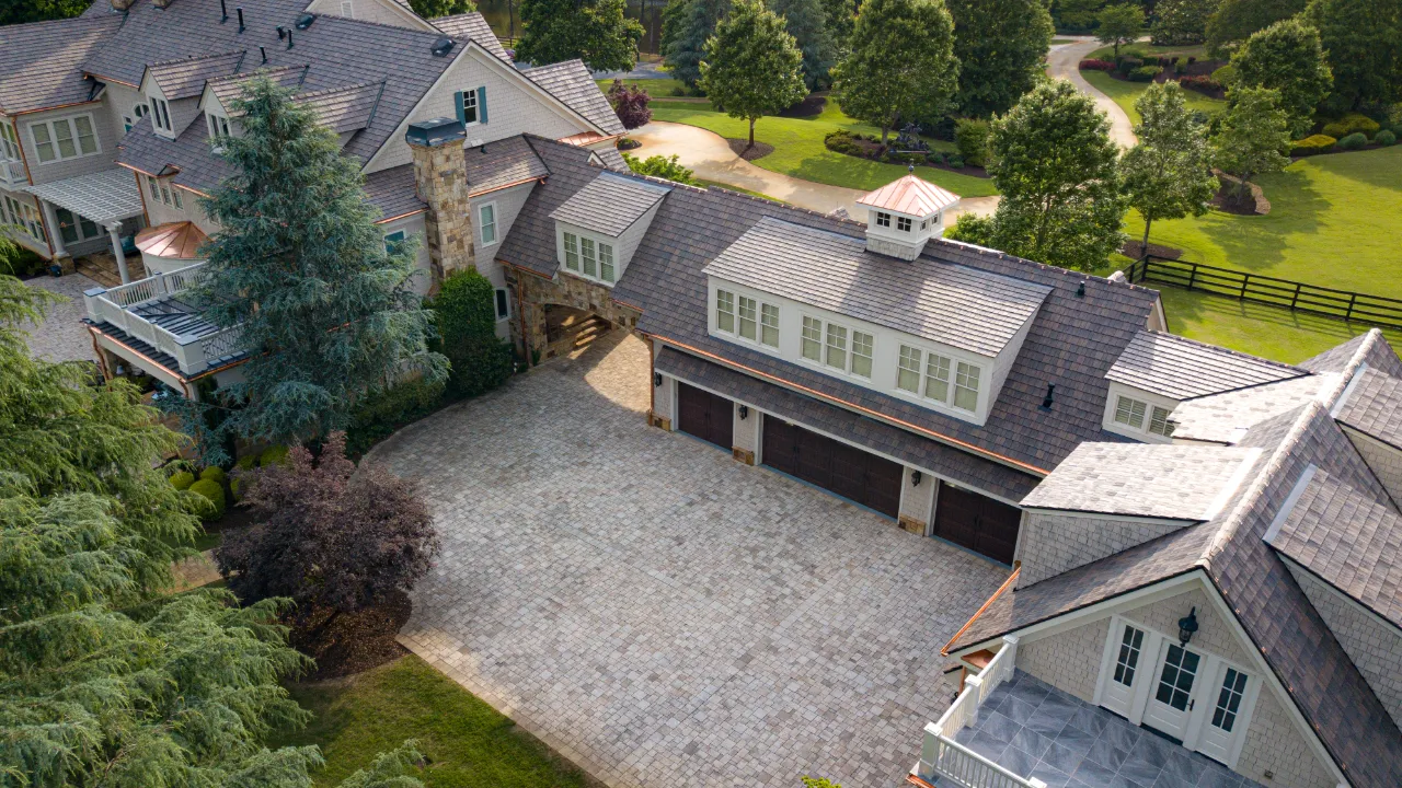 Aerial view of a large stone house with a gravel courtyard and surrounding trees and lawn