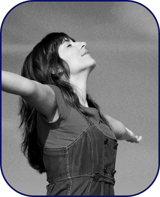 A young woman stands with her head held high, eyes closed, and arms stretched outward.