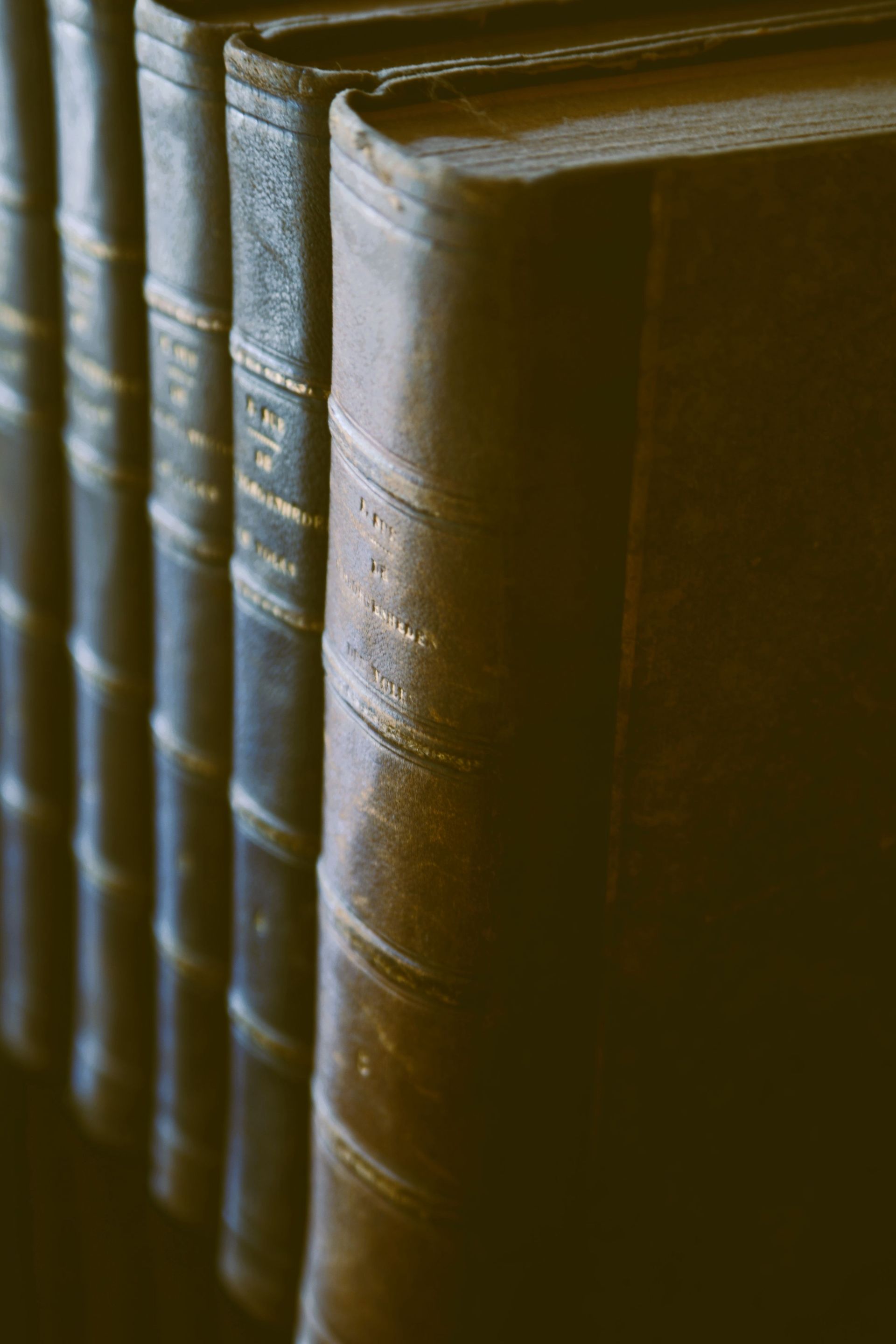 Row of worn brown hardcover books on a shelf, lit by warm light