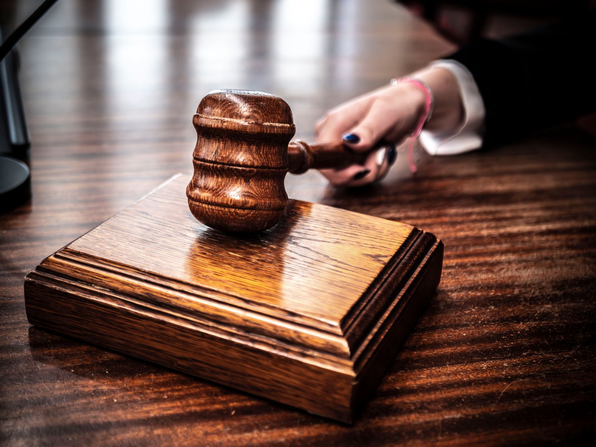 Judge's gavel on a wooden block with a hand in the background on a desk