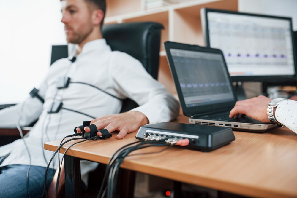 Man reclining in an office chair with a monitoring device attached, beside a laptop and computer setup