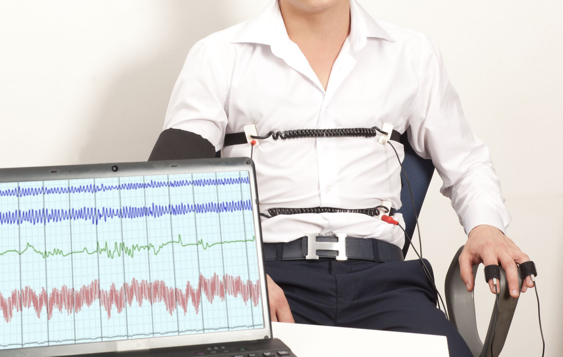 Person seated with a chest strap device beside a laptop displaying multicolored waveform charts