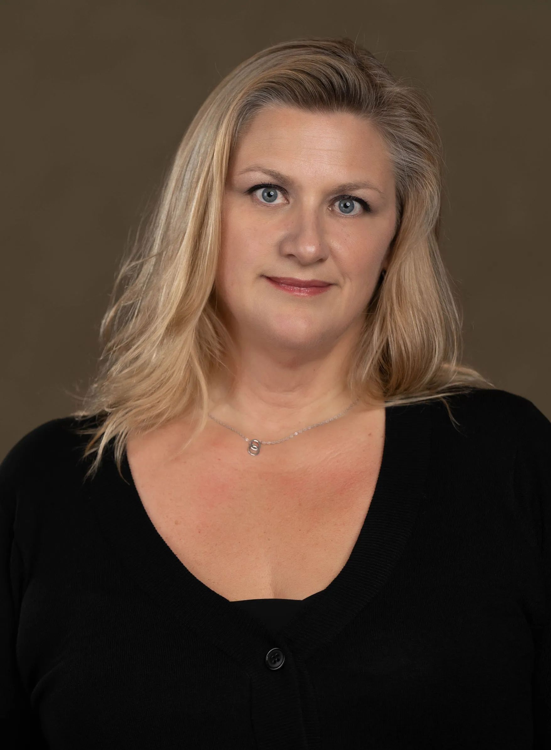 A woman with blonde hair is wearing a black shirt and a necklace.