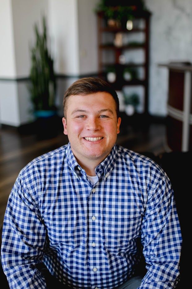 A man in a blue and white plaid shirt is smiling for the camera.