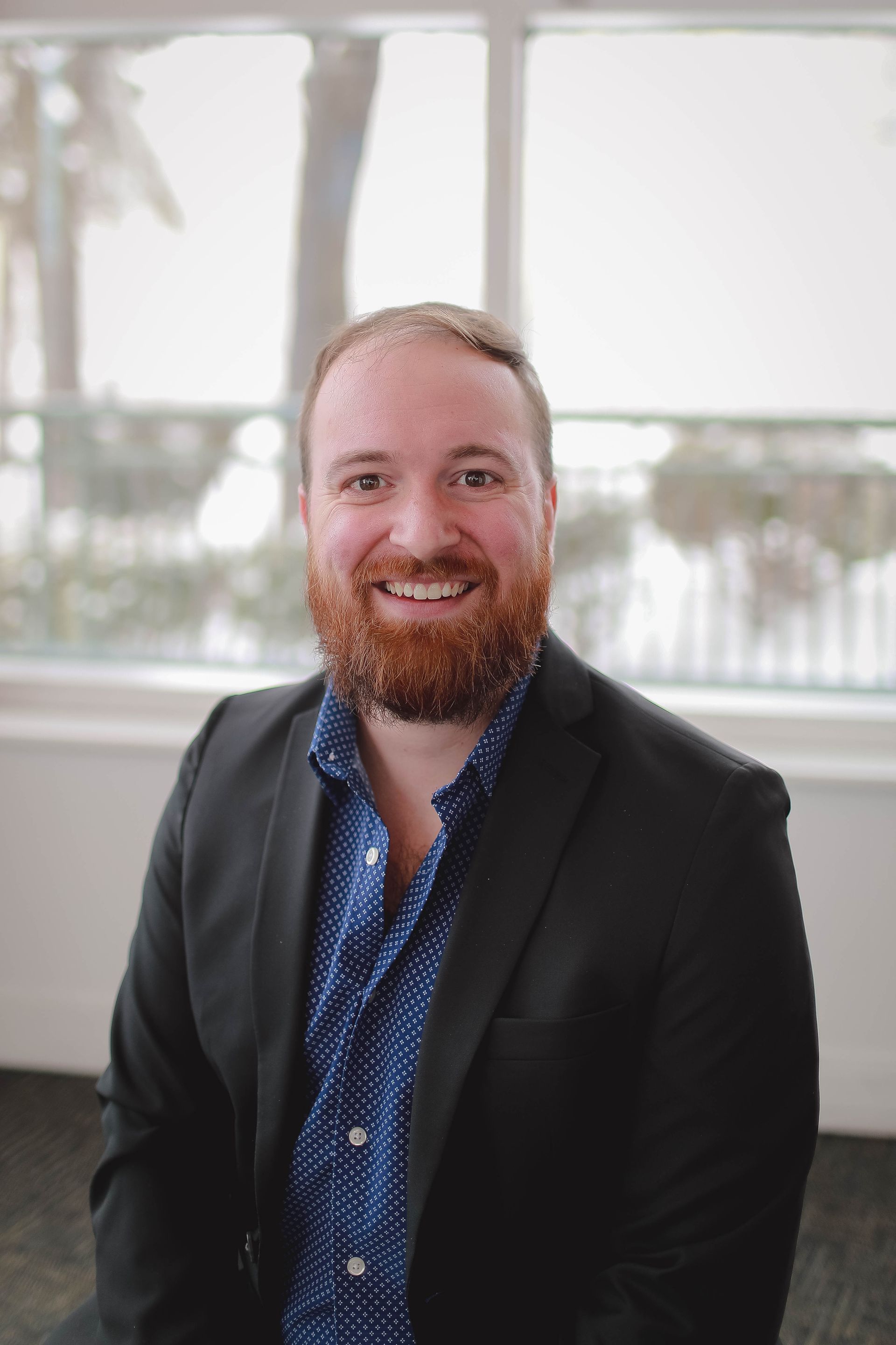 A man with a beard is wearing a blue shirt and smiling for the camera.