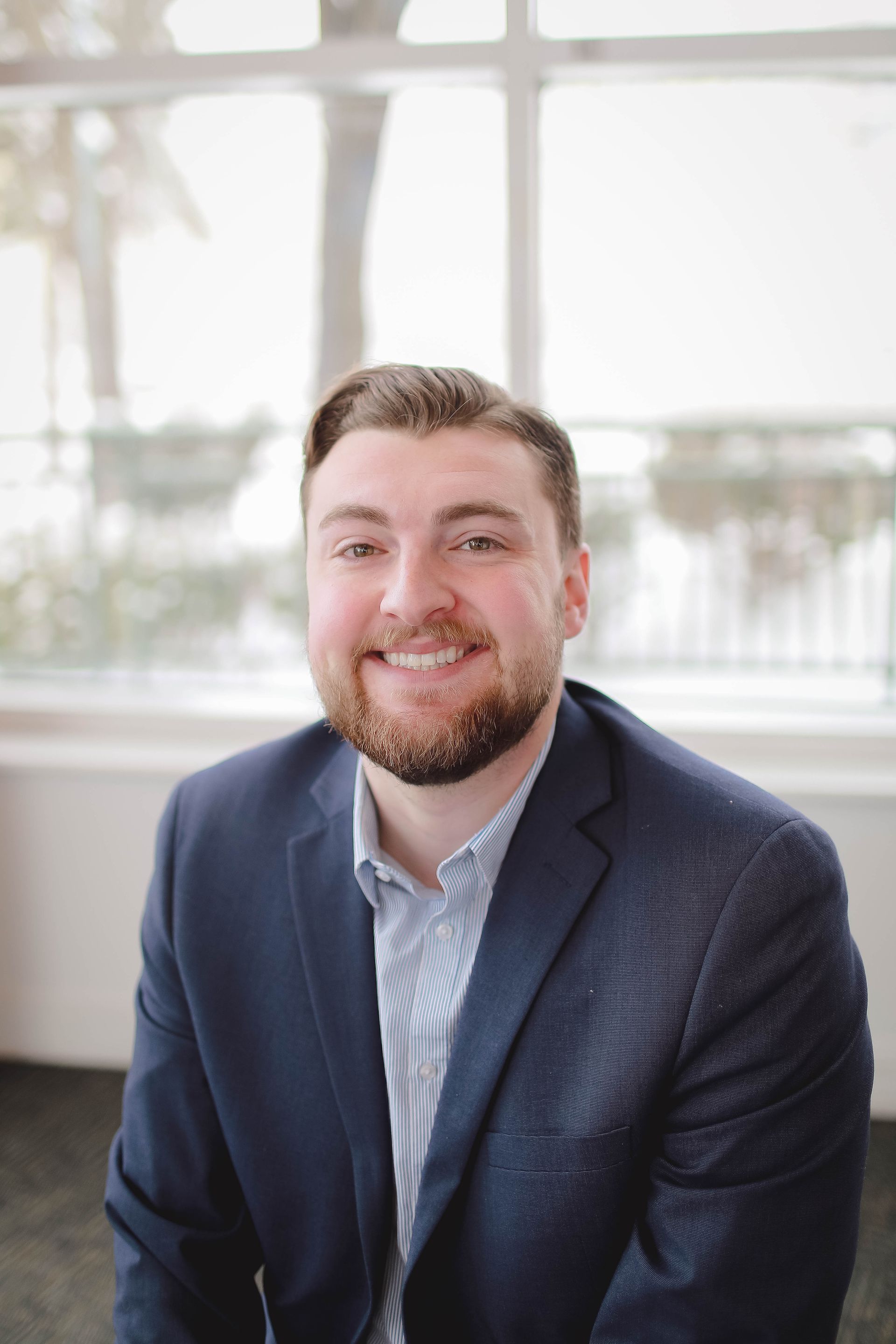 A man with a beard is smiling for the camera while wearing a tan polo shirt.
