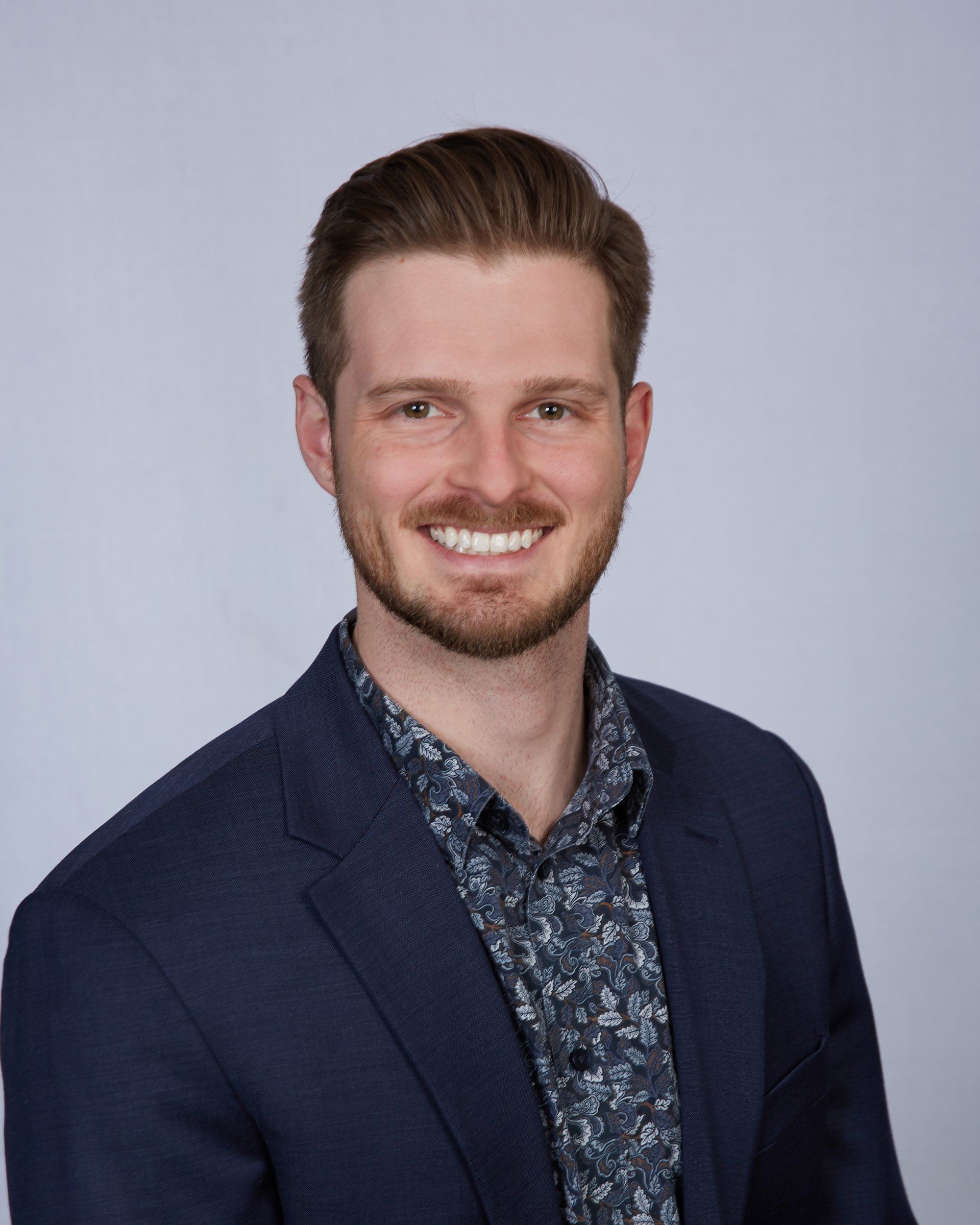 A man in a suit and floral shirt is smiling for the camera.