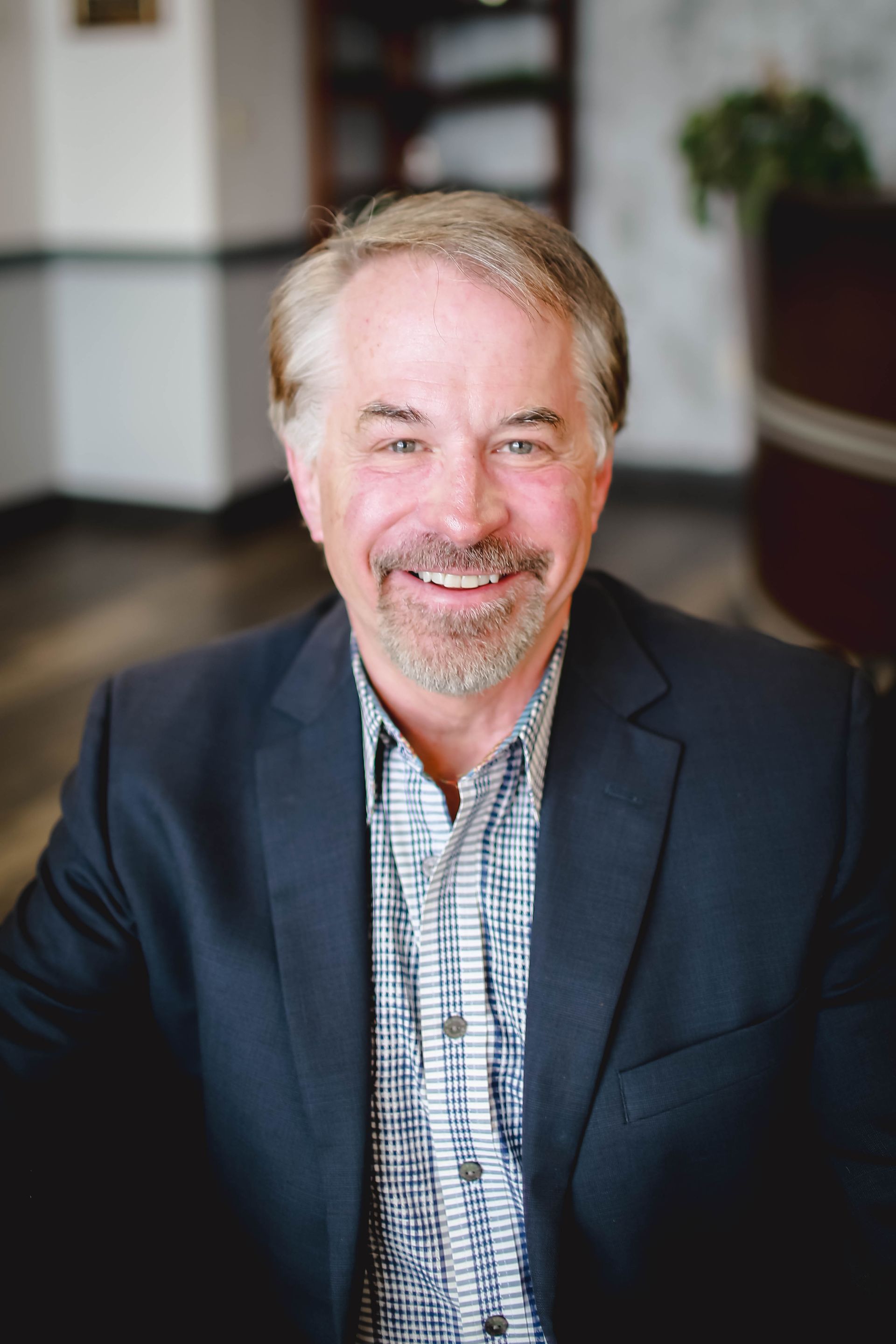 A man with a beard is wearing a plaid jacket and white shirt