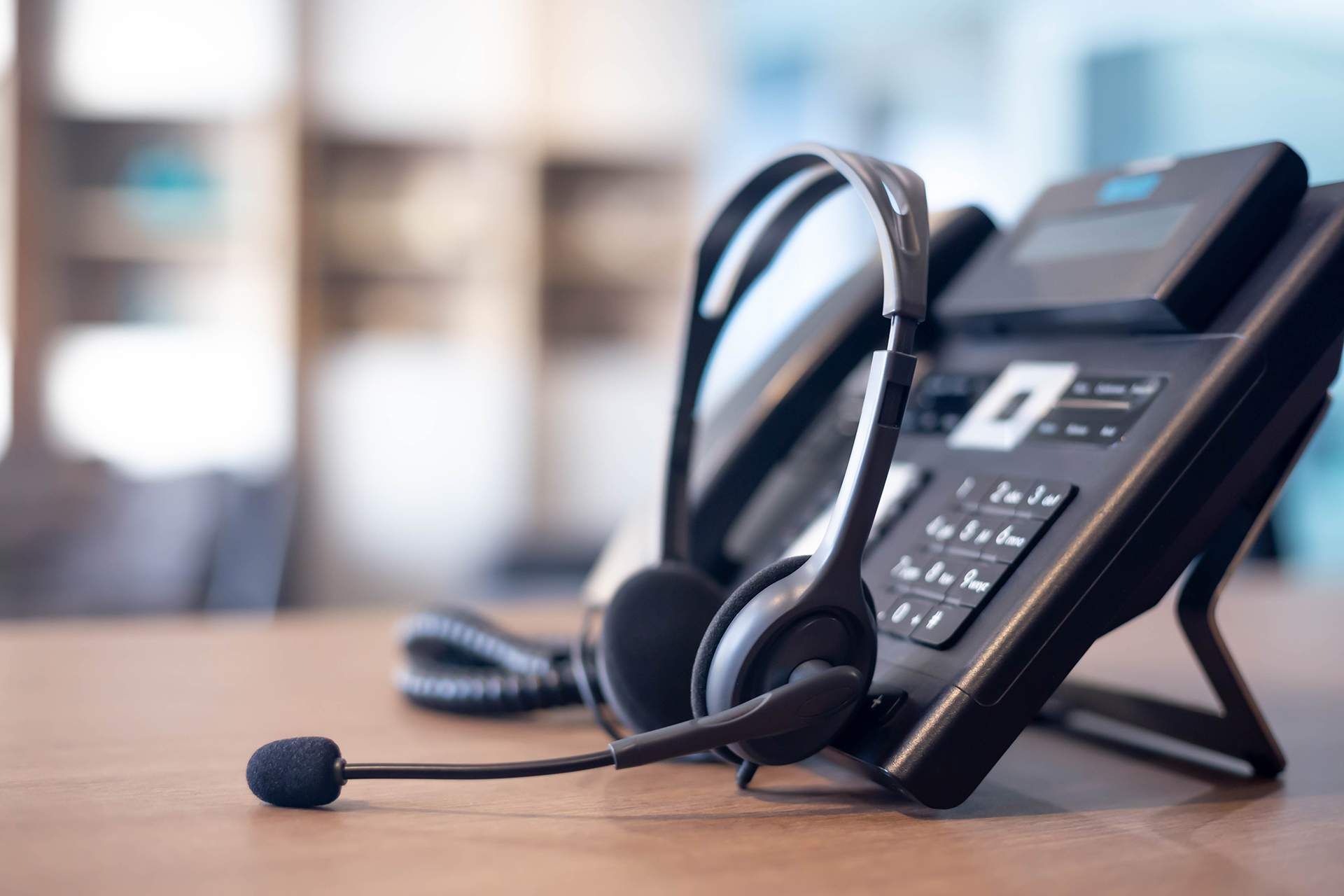 A headset is sitting next to a telephone on a table.