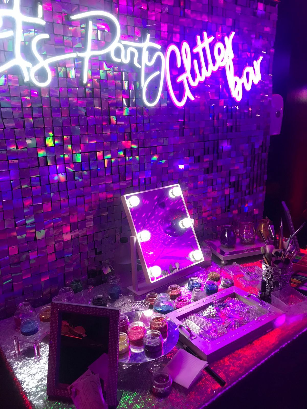 Barra de brillo con letrero de neón, pared brillante, espejo iluminado y suministros de maquillaje.