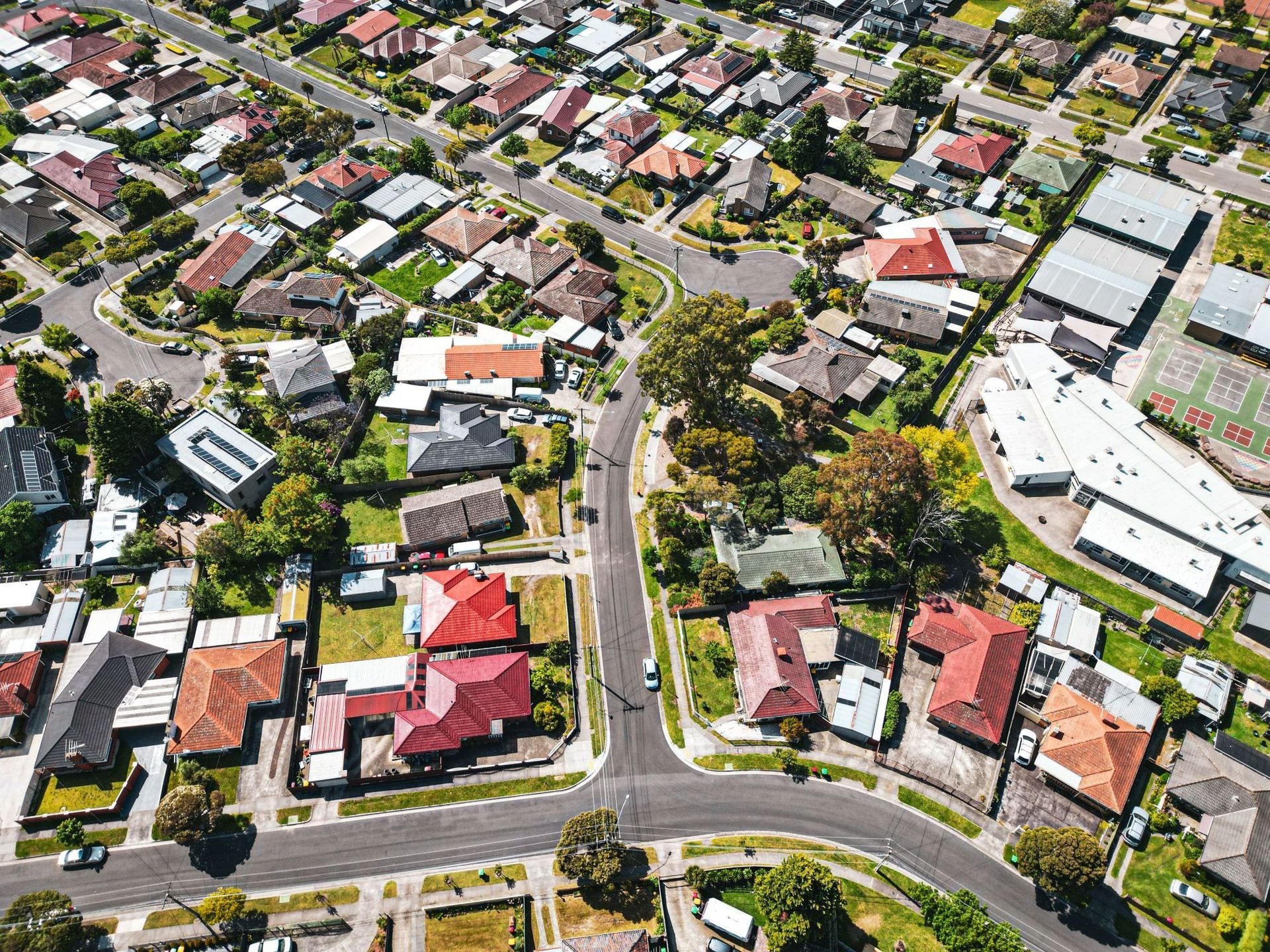 Aerial view of a suburban neighborhood with houses, roads, and trees under bright daylight.