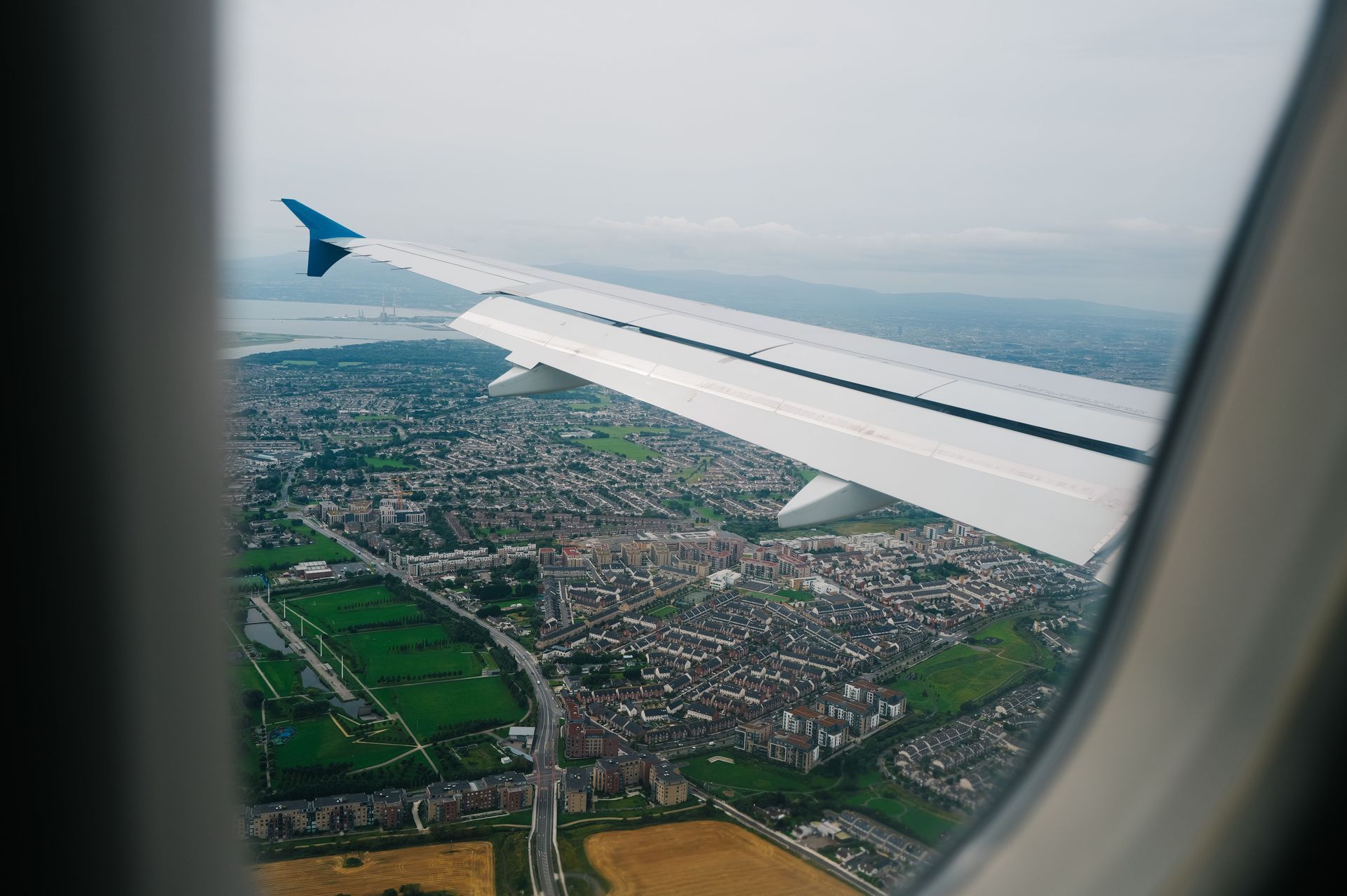 Airplane wing view over a city and green fields through a window