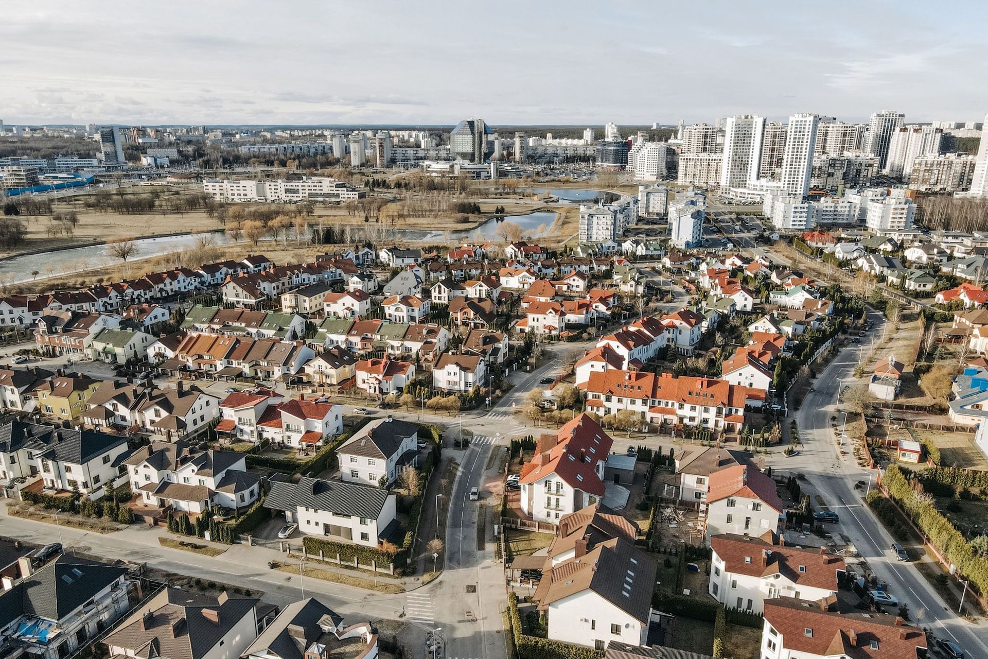 Aerial view of a suburban neighborhood with red-roofed houses and apartment buildings near open fields