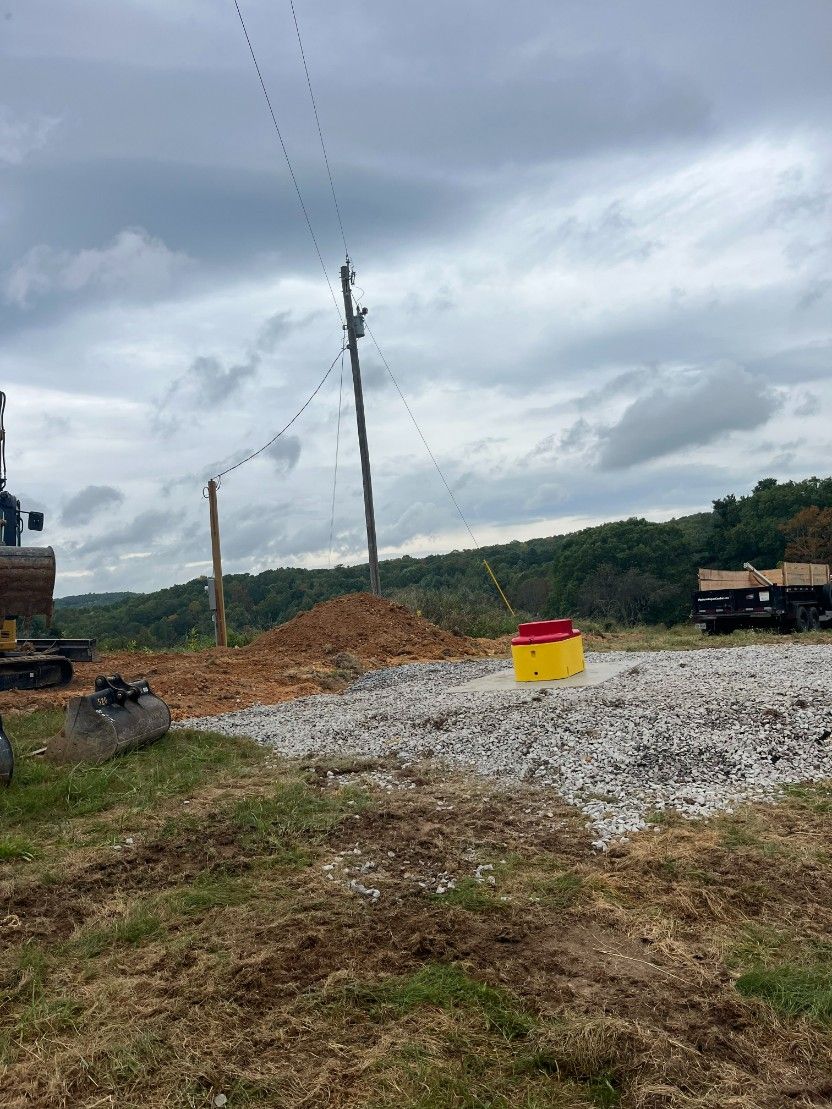 Construction site with utility poles, power lines, and piles of dirt and gravel under a cloudy sky.