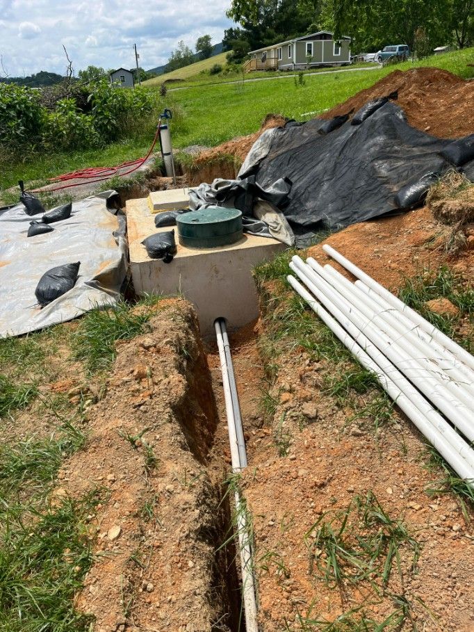 Trench with white pipes leading from a concrete septic tank in a grassy yard.