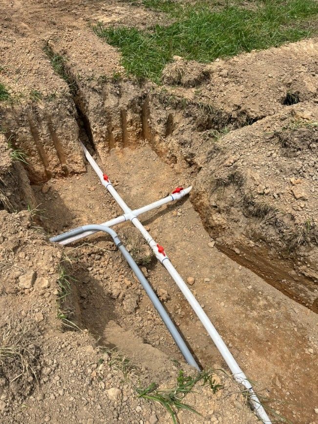 Trenches with white PVC pipes and red valves installed in the ground.
