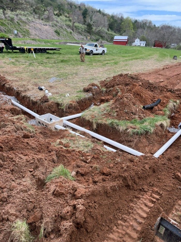 Construction site with buried white pipes in trenches; person standing near a truck in a field.