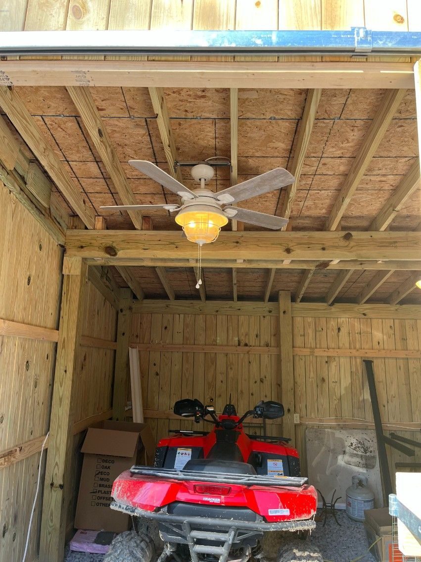 Red ATV parked inside a wooden shed with a ceiling fan.