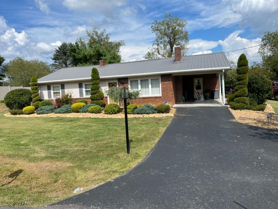 Ranch-style brick home with gray metal roof, covered carport, and well-manicured landscaping and driveway.