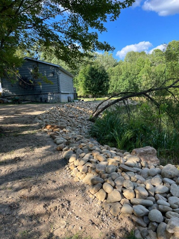 A rock-lined path next to a building and stream on a sunny day.
