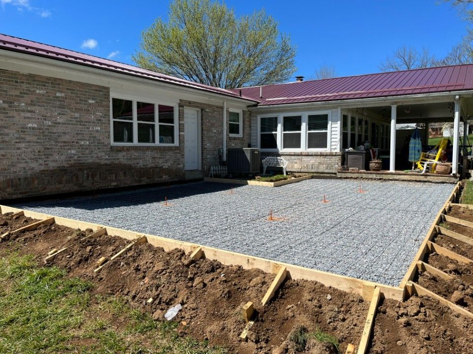 Gravel patio under construction next to a brick house with a red metal roof.