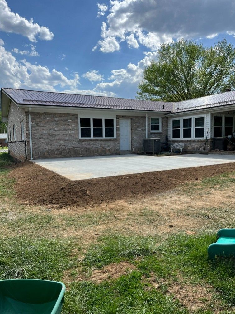 New concrete patio next to a brick building with a metal roof, on a sunny day.