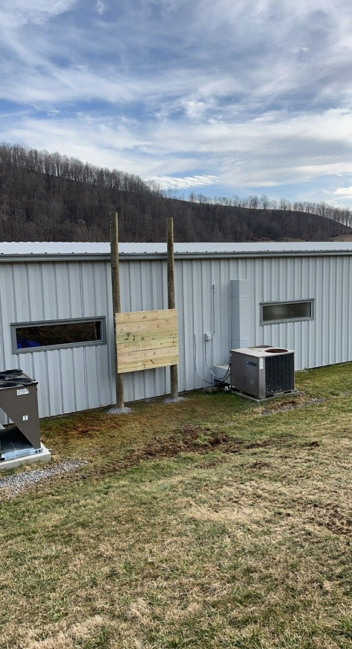 Exterior view of a metal building with wooden posts and a small ramp-like structure. Grass and trees in the background.