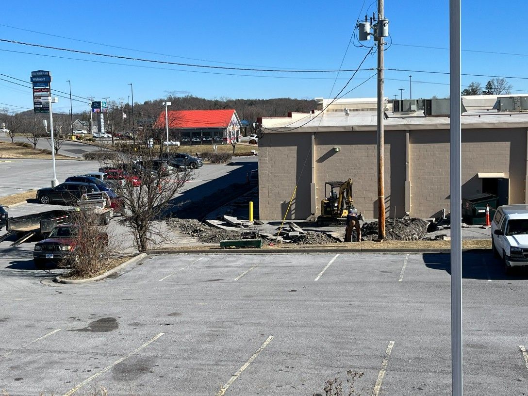 Parking lot with damaged building, construction activity, and nearby businesses under a sunny sky.